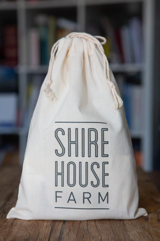 A cotton branded bag, tied at the top, resting on a wood surface with a bookshelf behind