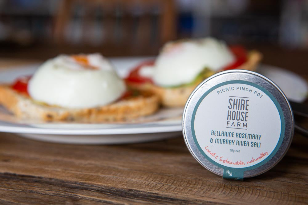 A tin resting against a white plate of eggs on toast, on a wood surface