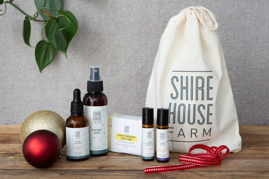 Rosemary water, rosemary oil, soap and two roll on bottles, all next to a cotton drawstring pouch, on a wood surface with Christmas baubles 