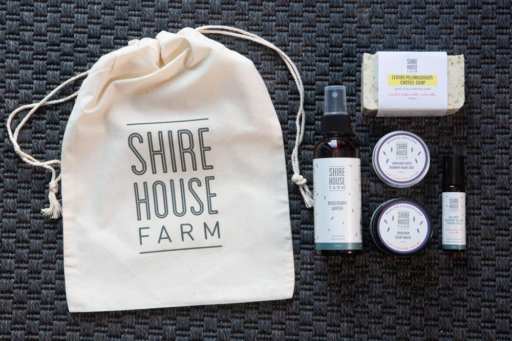 A cotton branded bag with self care products to the right, on a dark blue textured mat