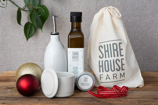 A bottle of olive oil next to a ceramic oil pourer, both sitting behind a salt tin and ceramic condiment pot. Displaying a cotton pouch for the products, and some Christmas decorations