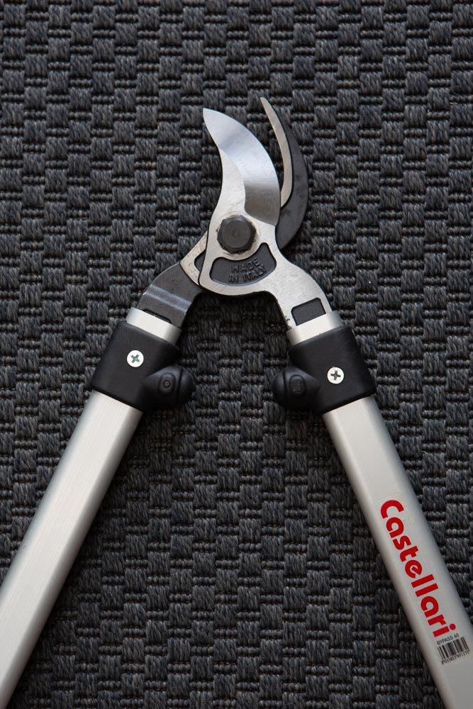 close up of bypass lopper blades and handles. Slightly open, on a dark grey textured mat