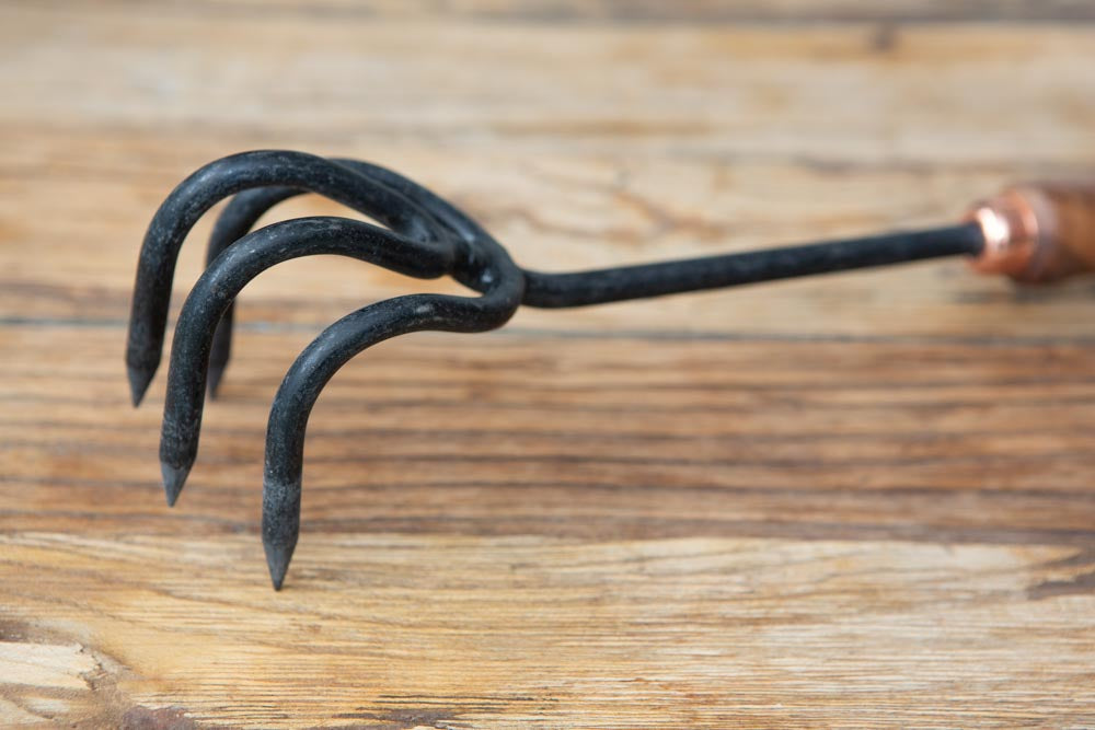 close up of the head of a stainless steel garden cultivator hand tool, resting on a wooden surface