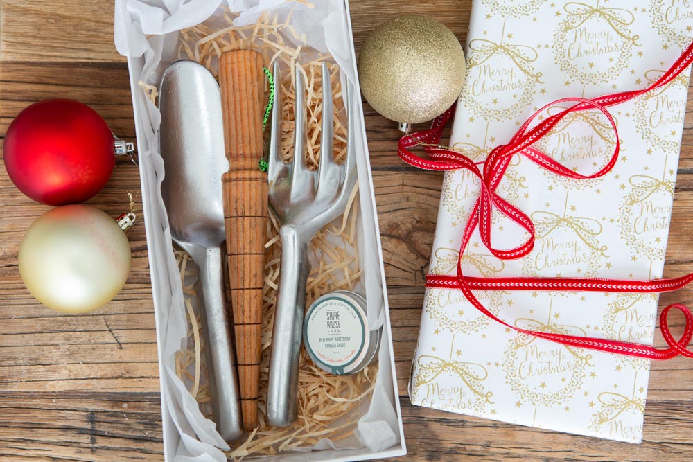 Christmas themed gift set of gardning tools, a trowel, fork, dibber and hand balm in a box with Christmas decorations around it