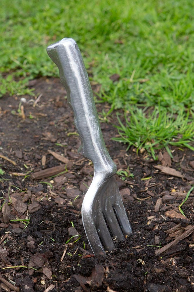 A metal garden fork dug into the dirt, with grass in the background