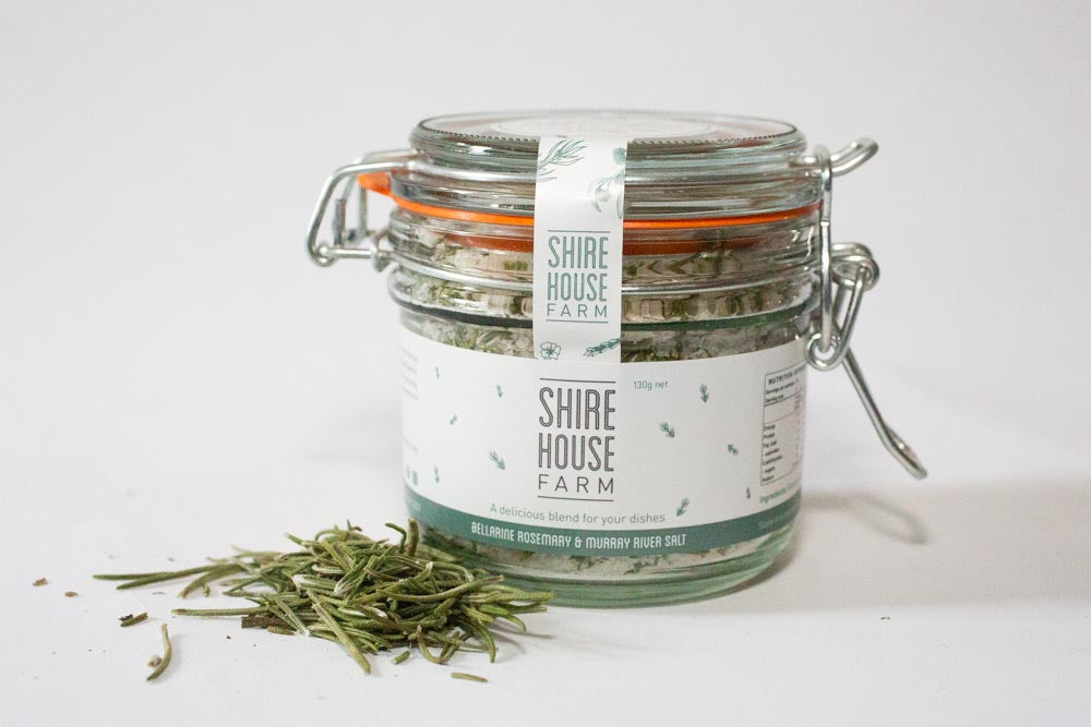 A clip top jar with a sprinkle of rosemary leaves on the side, with a white background