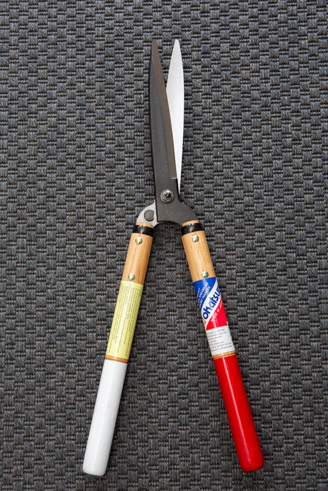 hedge shears with red and white handles, slightly opened, resting on a dark grey textured mat