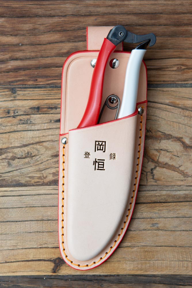 Beige holster with red and white secateurs inside, resting on wood surface