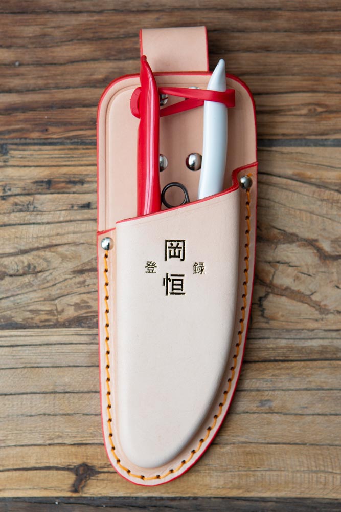 Beige holster with red and white garden snips inside, on wood surface