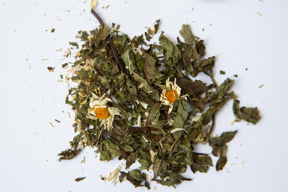 a pile of dried mint leaves and chamomile flowers, on a white surface