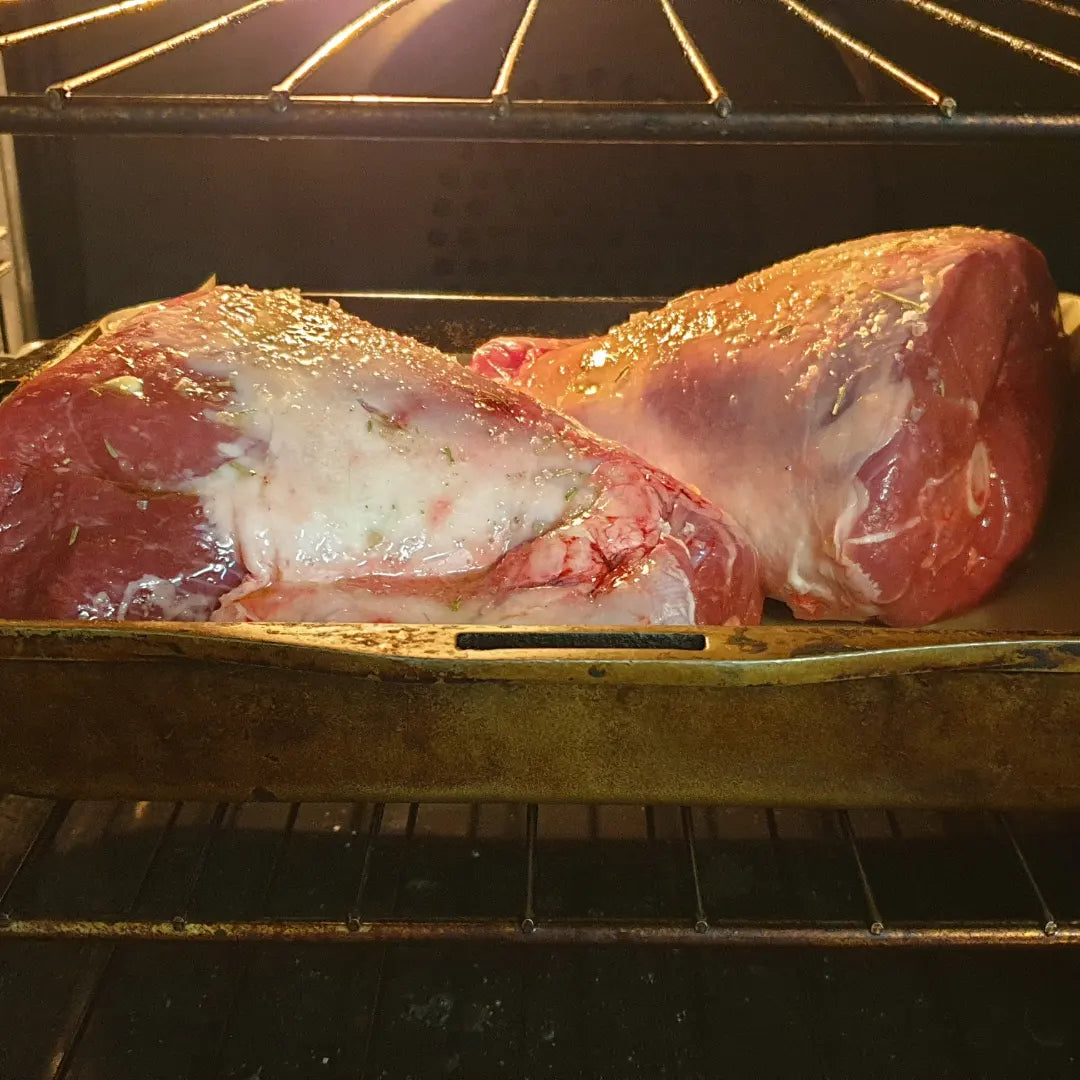 two legs of uncooked lamb in an oven