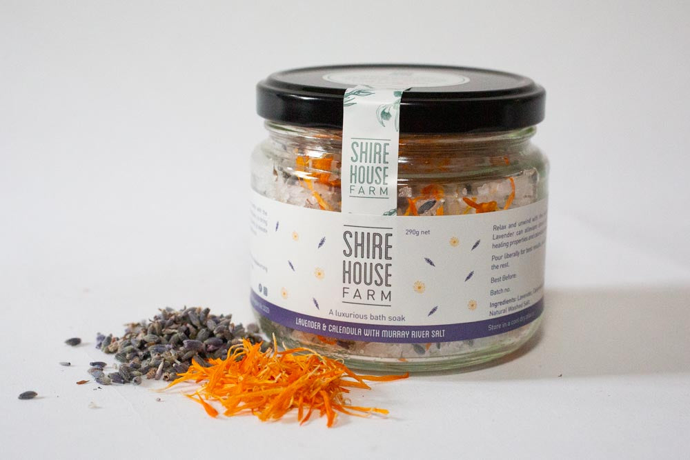 A glass jar filled with bath salt. A sprinkle of flower petals next to it, on a white background