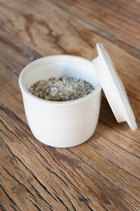 Ceramic salt dish filled with salt, with the lid resting on the side, on a wood surface