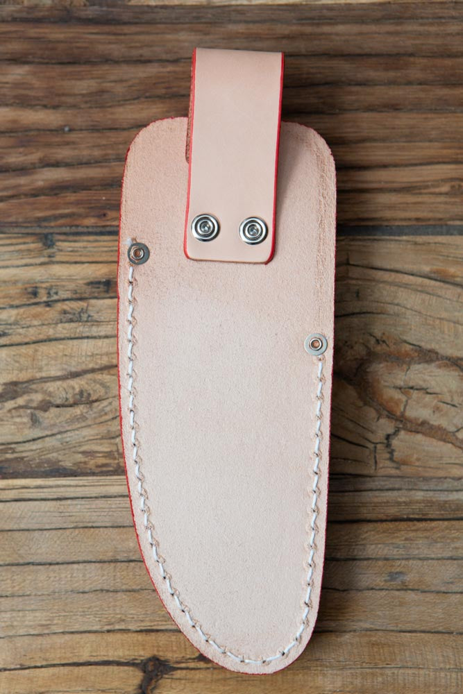 The back side of a beige holster for secateurs, on a wood surface