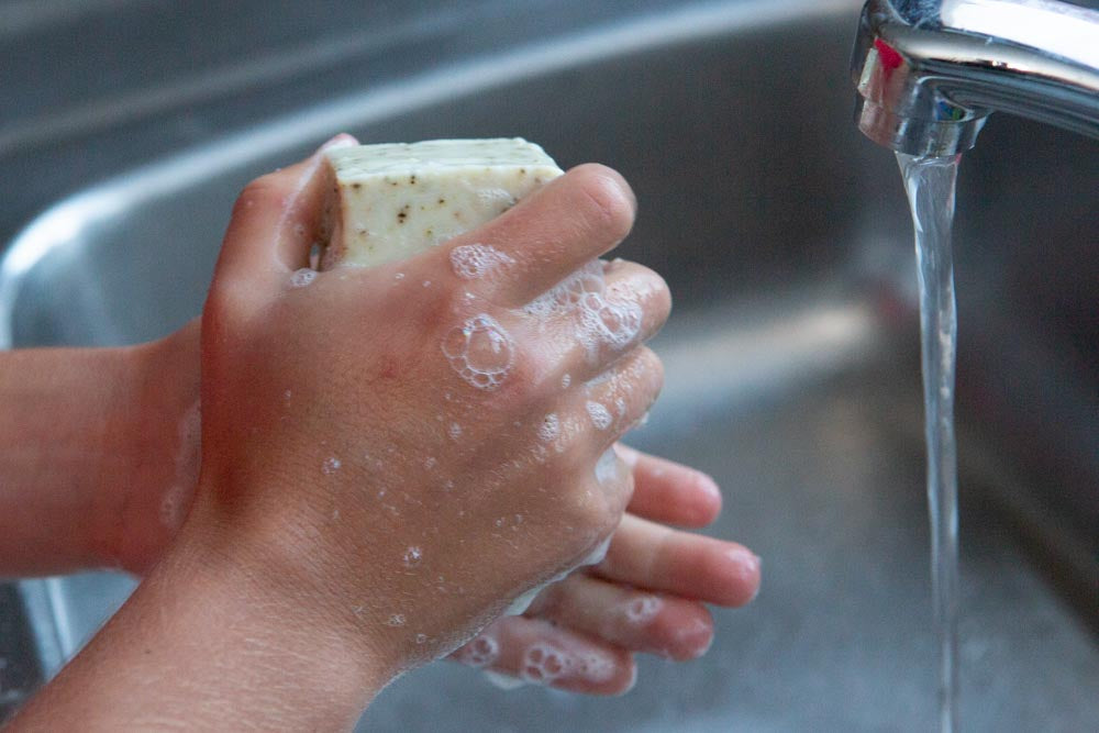 A child washing hands with soap next to a running tap