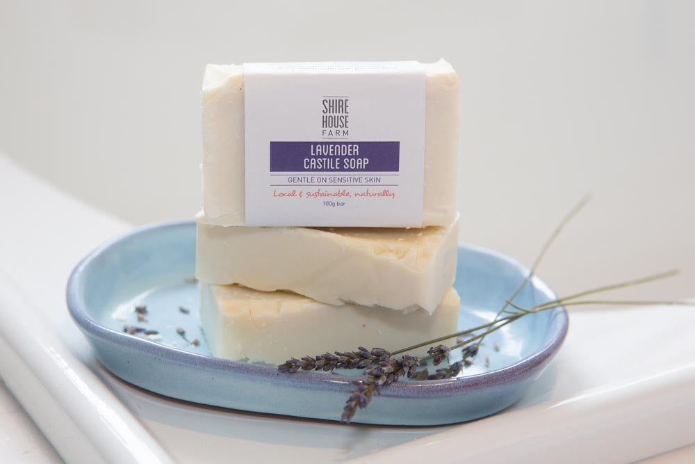 A stack of three soap bars in a blue dish with sprigs of lavender, on a white bath edge