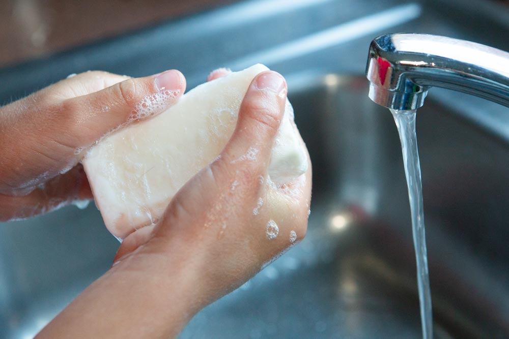 A child washing hands with a bar of soap, next to a running tap