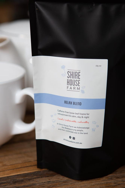 black pouch with white branded label, next to a blurred white teapot and mug, on a wood surface